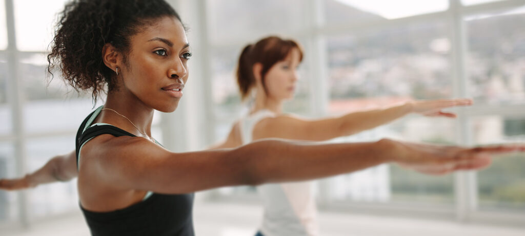 two women standing in warrior pose in a yoga class
