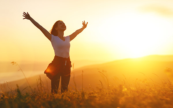 woman standing outside at sunset with her arms raised up and out