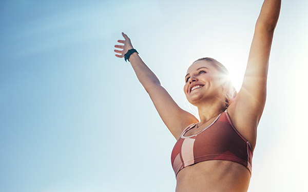 smiling woman outside with her arms raised to the sky