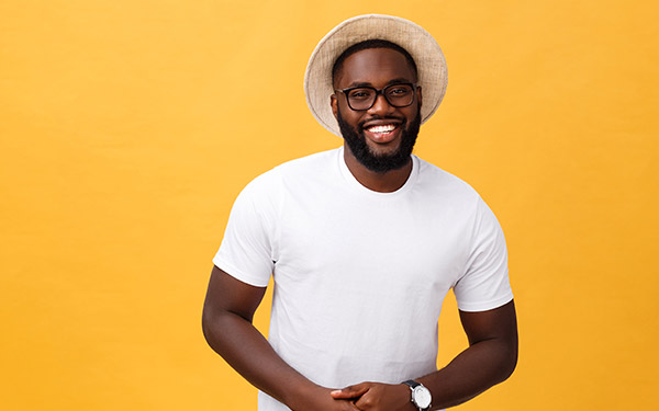 black man smiling in a fedora standing in front of a yellow background