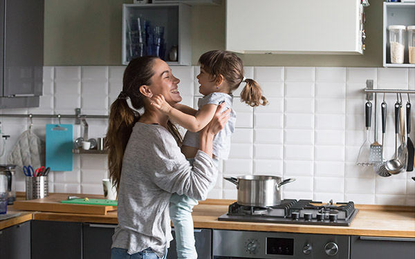 Image of a mom lifting her daughter in the kitchen.