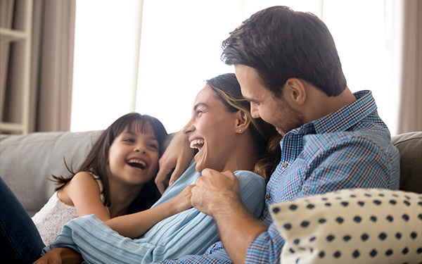 Image of mom and dad on the couch with their daughter.