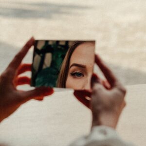 woman's eye is visible in small mirror she holds in front of her