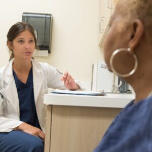 woman sits looking at doctor in exam room